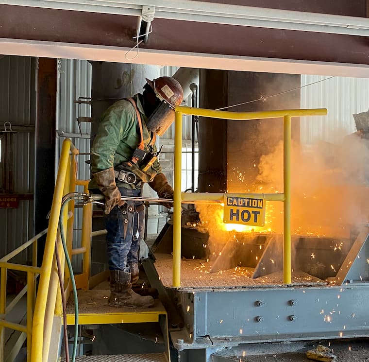 Worker beside a CAUTION HOT sign while hot work is under way