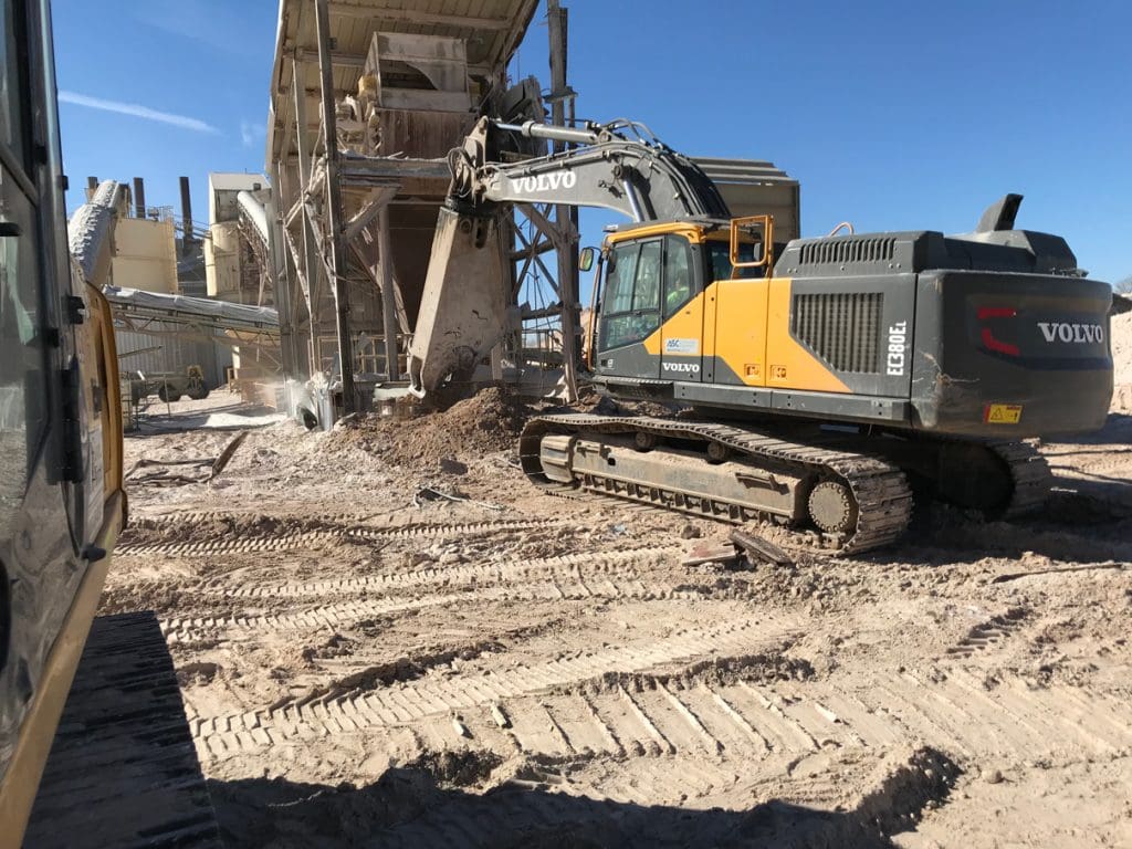 Excavator working in a cleared area beside plant buildings