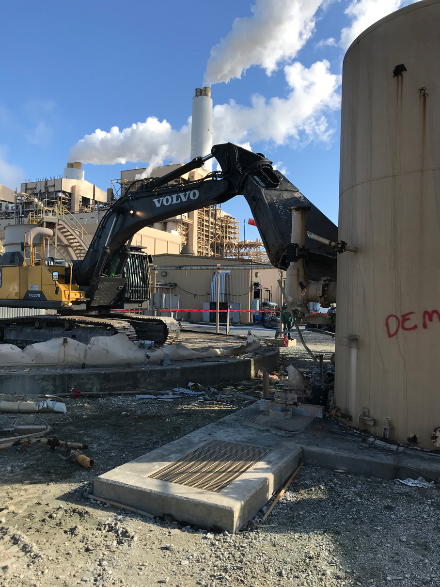 Excavator working beside an industrial structure