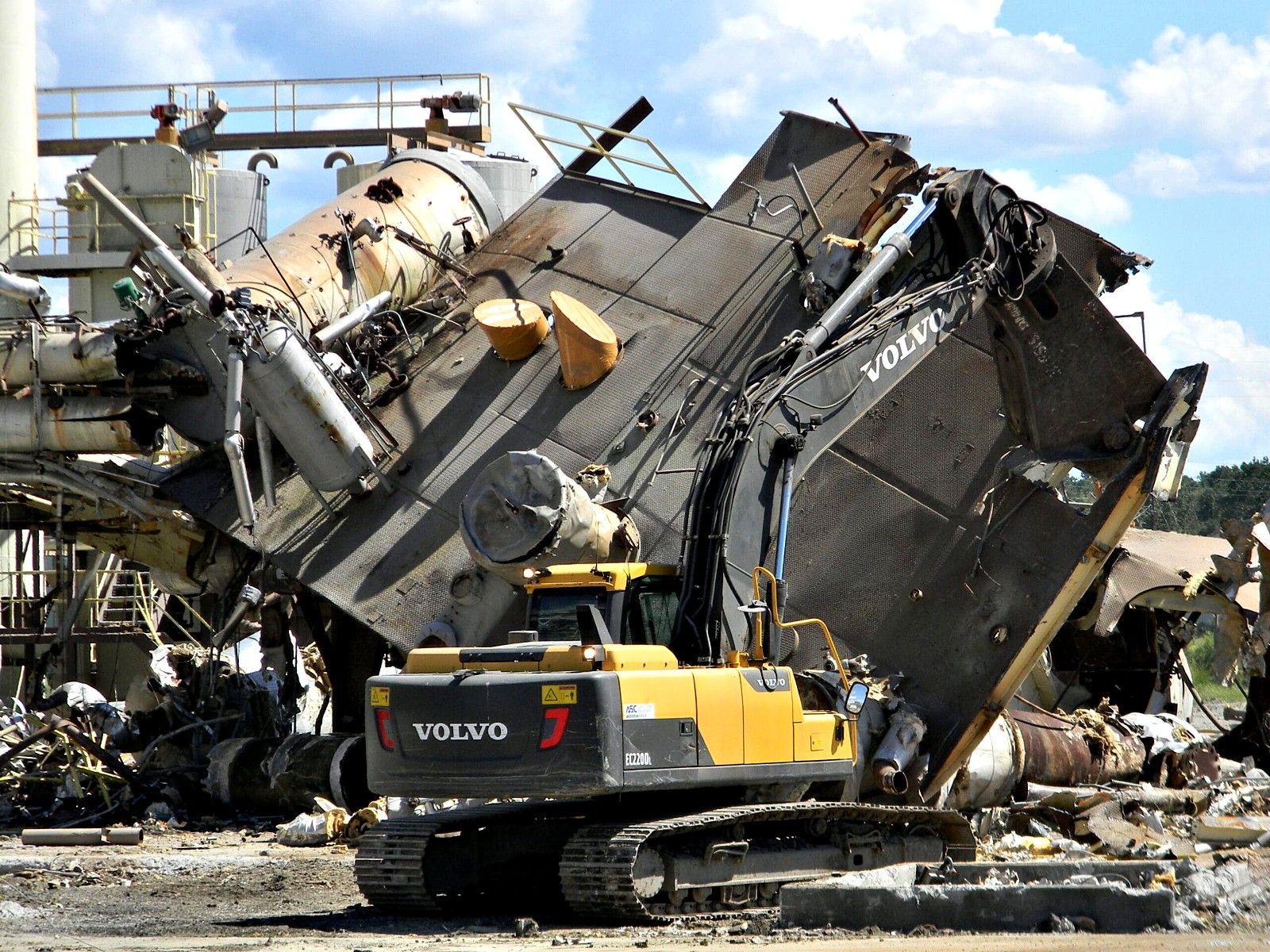 Excavator working beside a collapsing industrial plant roof