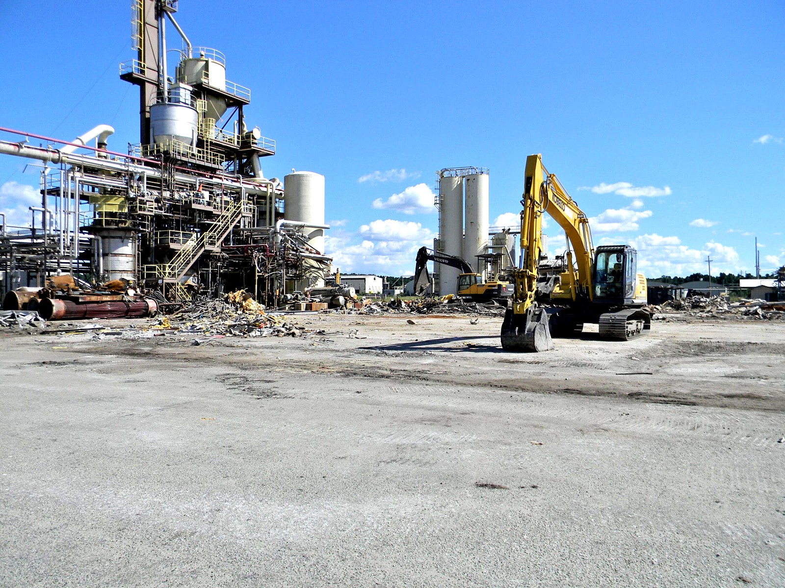 Excavator working at a process plant site with neighboring structures